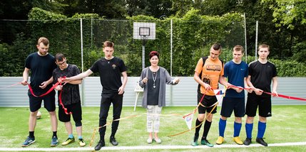 Junge Menschen stehen auf dem Fußballfeld. Eine Frau hat ein Band zur Einweihung des Feldes durchtrennt.